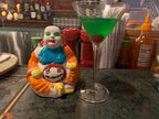 Colorful figurine next to a cocktail glass with green liquid on a bar counter.