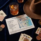 Map of a bar crawl route in Chicago with a glass of whiskey, hat, and playing cards on a dark surface.