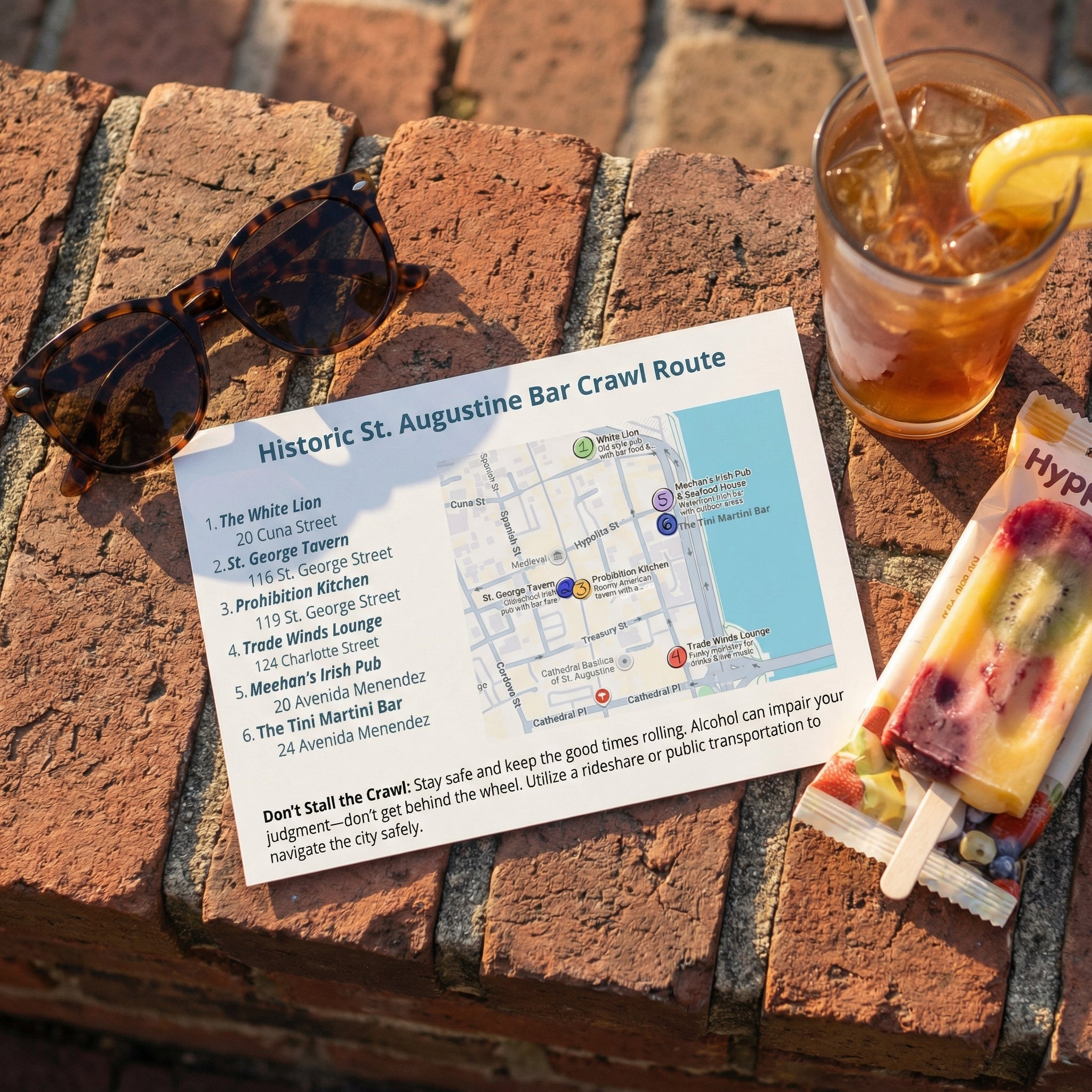 Map of Historic St. Augustine Bar Crawl Route on a brick surface with sunglasses, iced tea, and popsicles.